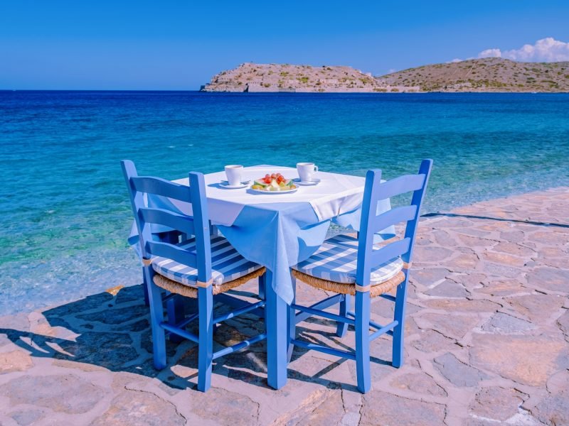 Plaka Lassithi village with traditional blue table and chairs and the beach in Crete Greece